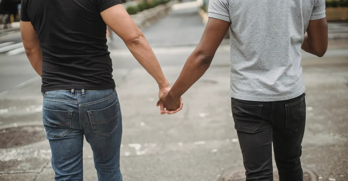 Back view of two men holding hands on an outdoor walk