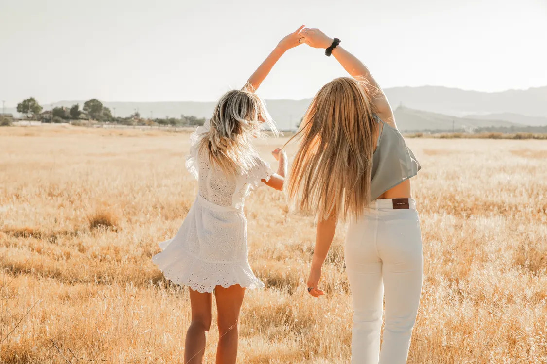 Back view of two women holding hands in a sunlit golden field